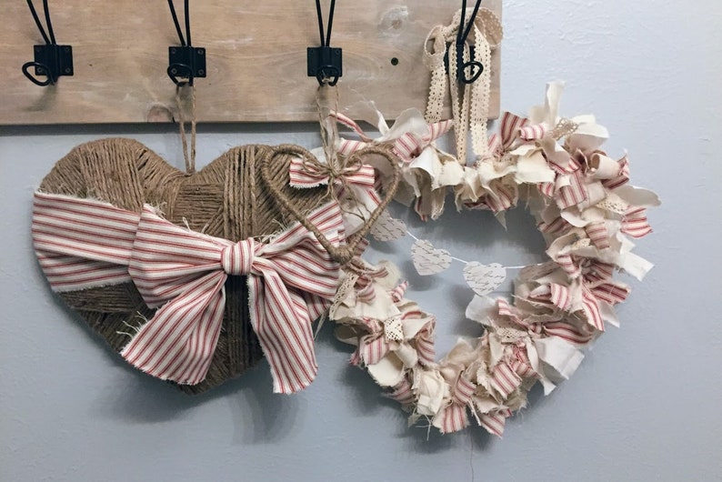 May include: Two heart-shaped wreaths, one made of burlap with a red and white striped bow, and the other made of white fabric with red and white striped accents.