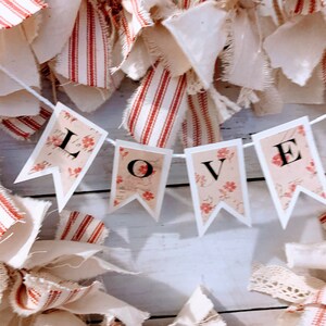 May include: A white and red striped fabric wreath with a banner that reads "LOVE" in black letters. The banner is made of white paper with a floral pattern and each letter is on a separate pennant.