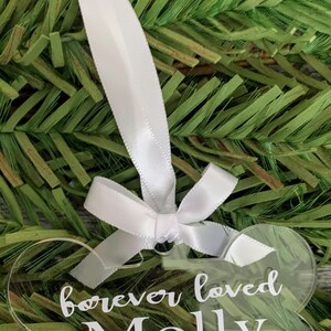 May include: A clear acrylic dog bone ornament with the text "forever loved Molly 2002 - 2013" engraved on it. The ornament is hanging from a white ribbon.