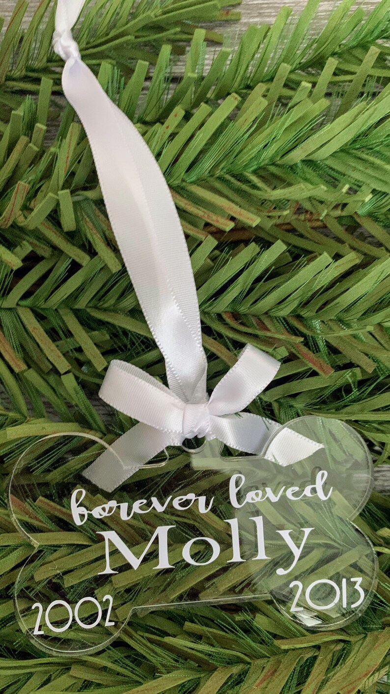 May include: A clear acrylic dog bone ornament with the text "forever loved Molly 2002 - 2013" engraved on it. The ornament is hanging from a white ribbon.
