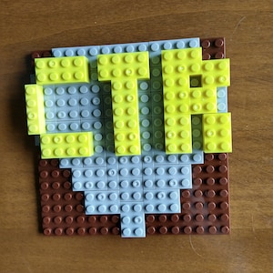 May include: A close-up of a LEGO® brick model of the word "CTR" in yellow letters on a gray and brown base.