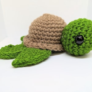 May include: A crocheted turtle toy with a brown shell and green body. The turtle has a black button eye.