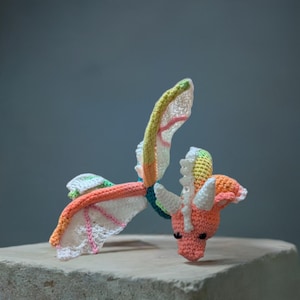 May include: A crocheted dragon toy with a pink head, white wings, and a rainbow-colored body.
