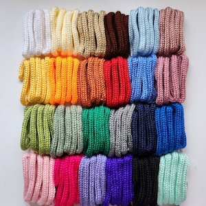May include: A collection of 20 spools of colorful waxed cotton cord. The cords are arranged in a grid pattern, with each spool containing a different color. The colors include white, yellow, orange, brown, red, blue, green, pink, purple, and black.