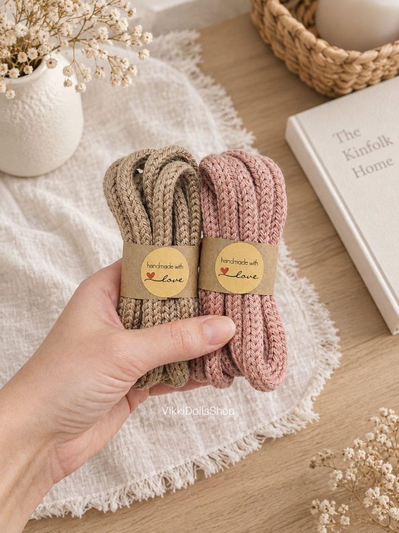 May include: Two bundles of thick, braided yarn cords in beige and dusty pink. Each bundle is secured with a tan paper label featuring the text "handmade with love" and a small red heart icon. The cords have a textured, knit-like appearance.