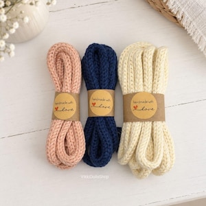 May include: Three bundles of thick, knitted cord in soft pink, navy blue, and cream. Each bundle is secured with a brown paper band featuring the printed text 'handmade with love' and a small red heart icon. The cords have a textured, braided appearance.