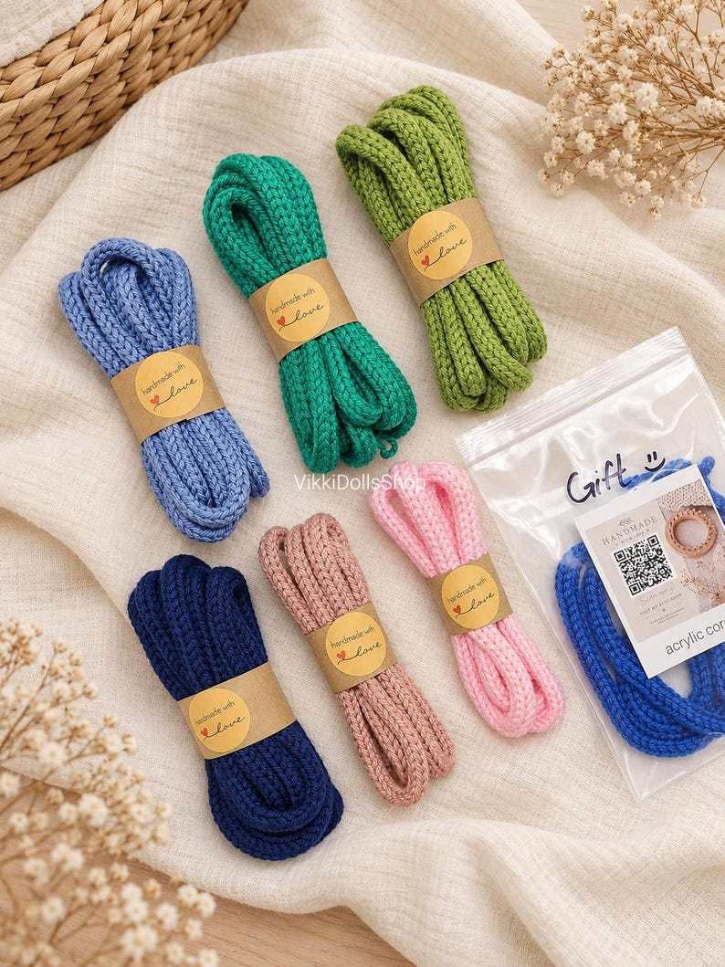 May include: Six bundles of braided acrylic cord in blue, green, lime, navy, dusty rose, and pink. Each bundle is wrapped in a brown paper band labeled "handmade with love" with a heart icon. One blue cord is inside a clear plastic gift bag.