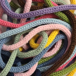 May include: A collection of multi-colored knitted cords tangled together. The cords feature a braided texture and come in various shades including pink, light blue, lavender, yellow, sage green, dark brown, and navy blue.