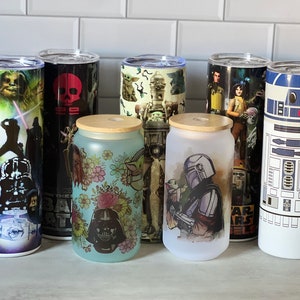 Op de afbeelding: Zeven verschillende Star Wars-bekers, waaronder een zwarte beker met een schedel en gekruiste beenderen, een witte beker met een R2-D2-ontwerp en een blauwe beker met een bloemenpatroon en Darth Vader.