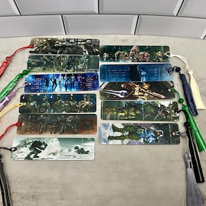 May include: A collection of rectangular bookmarks featuring various action scenes with characters in military-style armor. Each bookmark has a colorful tassel attached. The bookmarks are in shades of green, blue, and gray.