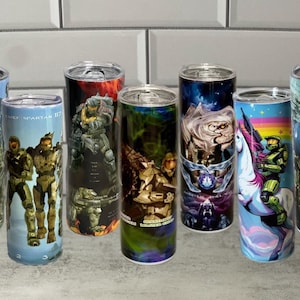 May include: A collection of eight stainless steel tumblers featuring various designs from the Halo video game series. The designs include characters, logos, and scenes from the game, with vibrant colors and detailed artwork. Each tumbler has a silver lid.