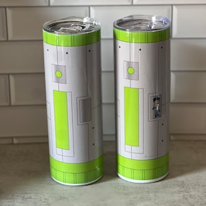 Pode incluir: Dois copos de aço inoxidável com um design geométrico cinza e verde. Um copo apresenta um personagem de desenho animado no design.