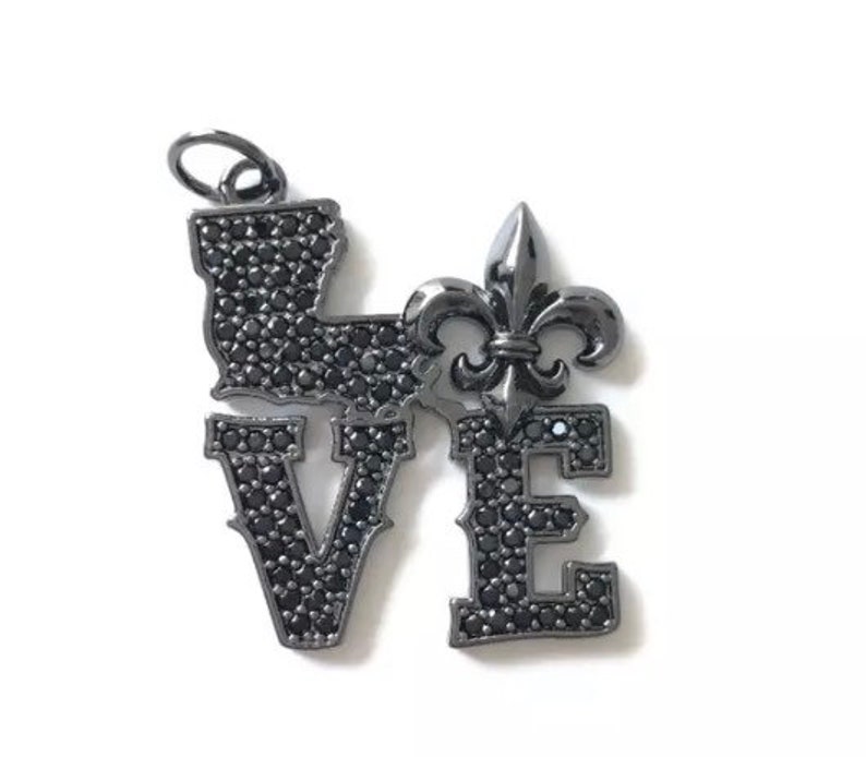 Pu&ograve; includere: Un ciondolo in metallo nero con la parola "LOVE" scritta in strass neri. La lettera "O" &egrave; sostituita da un design a giglio.