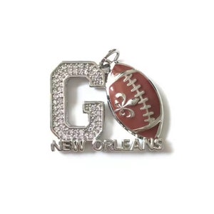 Pu&ograve; includere: Ciondolo in argento con una 'G' incrostata di strass e un pallone da calcio rosso con un design a giglio. Il ciondolo recita 'NEW ORLEANS'.