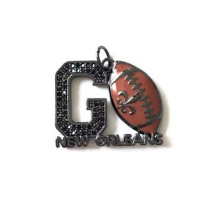 Pu&ograve; includere: Ciondolo in metallo nero con una lettera G incrostata di strass neri e un pallone da calcio marrone con un design a giglio. Il ciondolo recita "NEW ORLEANS".