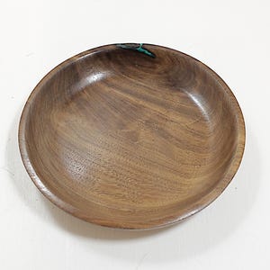 May include: A round wooden bowl, crafted from dark brown wood with a polished surface. The bowl features a smooth, curved design and a small turquoise inlay near the rim. This decorative bowl is ideal for serving food or as a decorative item.