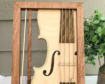 May include: A wooden framed wall art piece featuring a layered design of a violin. The violin is made of light and dark wood, with the strings and neck visible. The frame is a dark brown wood.