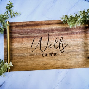 May include: A wooden serving tray with gold metal handles. The tray is engraved with the text "Wells Est. 2010".