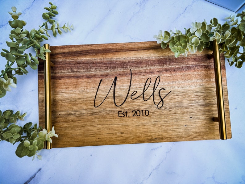 May include: A wooden serving tray with gold metal handles. The tray is engraved with the text "Wells Est. 2010".