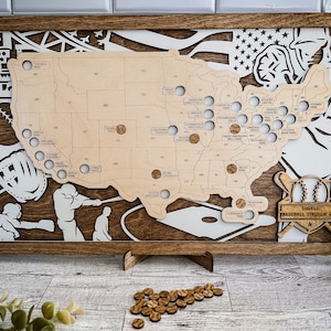 May include: A wooden map of the United States with baseball stadiums marked. The map is surrounded by a wooden frame and includes a baseball glove, a baseball bat, and a baseball. The text "Durkee Baseball Stadium Map" is at the bottom of the map.