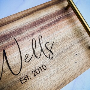 May include: A wooden serving tray with a gold metal handle. The tray has the words "Wells Est. 2010" engraved on the surface.