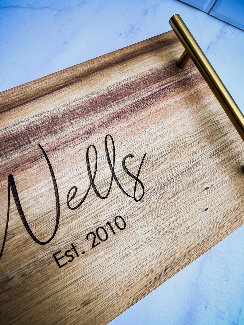 May include: A wooden serving tray with a gold metal handle. The tray has the words "Wells Est. 2010" engraved on the surface.