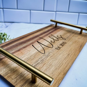 May include: A wooden serving tray with gold metal handles. The tray is engraved with the text "Wells Est. 2010".