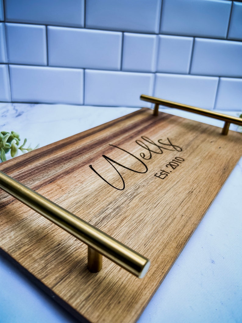 May include: A wooden serving tray with gold metal handles. The tray is engraved with the text "Wells Est. 2010".