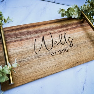 May include: A wooden serving tray with gold metal handles. The tray is engraved with the text "Wells Est. 2010".