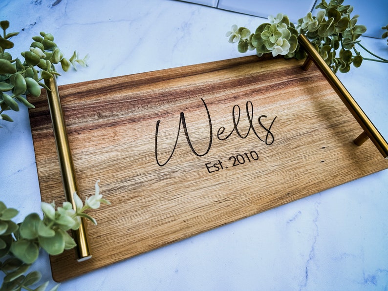 May include: A wooden serving tray with gold metal handles. The tray is engraved with the text "Wells Est. 2010".