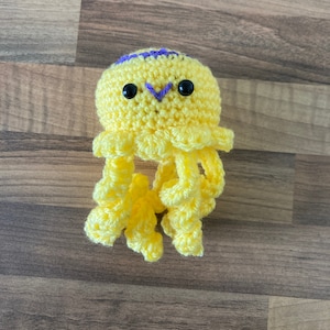 May include: A crocheted yellow jellyfish toy with purple accents and black eyes.