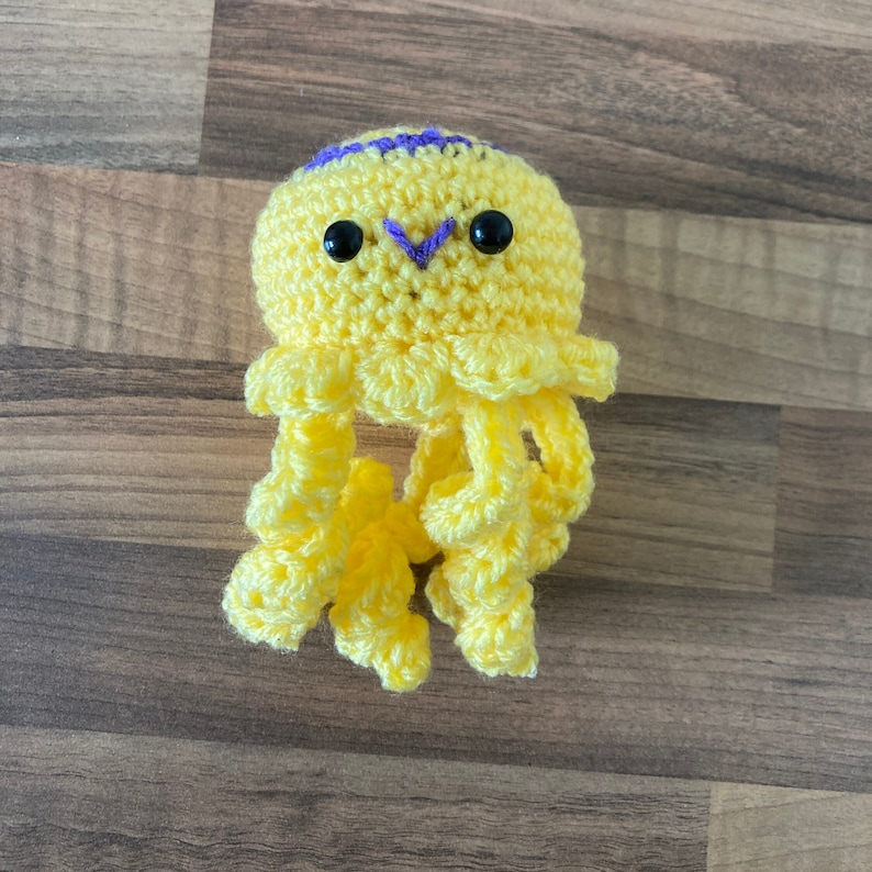 May include: A crocheted yellow jellyfish toy with purple accents and black eyes.