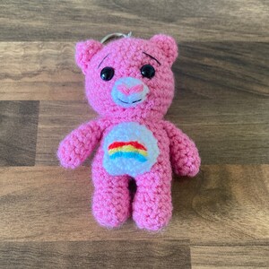 May include: Pink crocheted teddy bear keychain with a rainbow on its chest.
