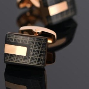 May include: A pair of black and rose gold cufflinks with a checkered pattern and a rose gold stripe.