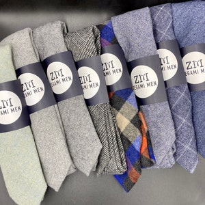 May include: A collection of ten neckties in various patterns and colors, including gray, blue, black, and white. The ties are all made of a soft, textured fabric and feature the text "Zimi Zegami Men" on the label.