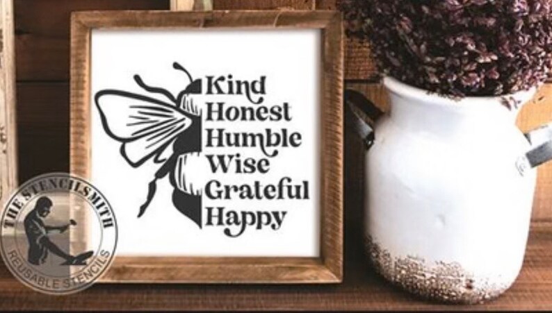 Puede incluir: Una plantilla en blanco y negro de una abeja con las palabras "Kind, Honest, Humble, Wise, Grateful, Happy" escritas verticalmente en el cuerpo de la abeja. La plantilla est&aacute; sobre un fondo blanco y est&aacute; enmarcada en un marco de madera.
