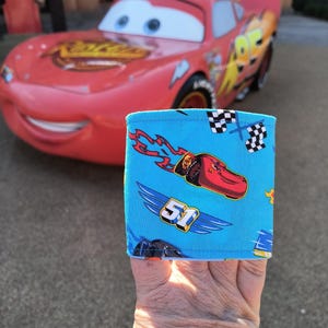 Pode incluir: Um bracelete de tecido azul com um carro de corrida vermelho e o número 51 nele. O bracelete tem uma bandeira quadriculada e chamas impressas.