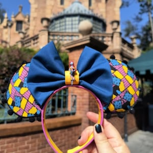 May include: A pair of blue and yellow patterned Minnie Mouse ears with a blue bow and a small Sally figure from The Nightmare Before Christmas.