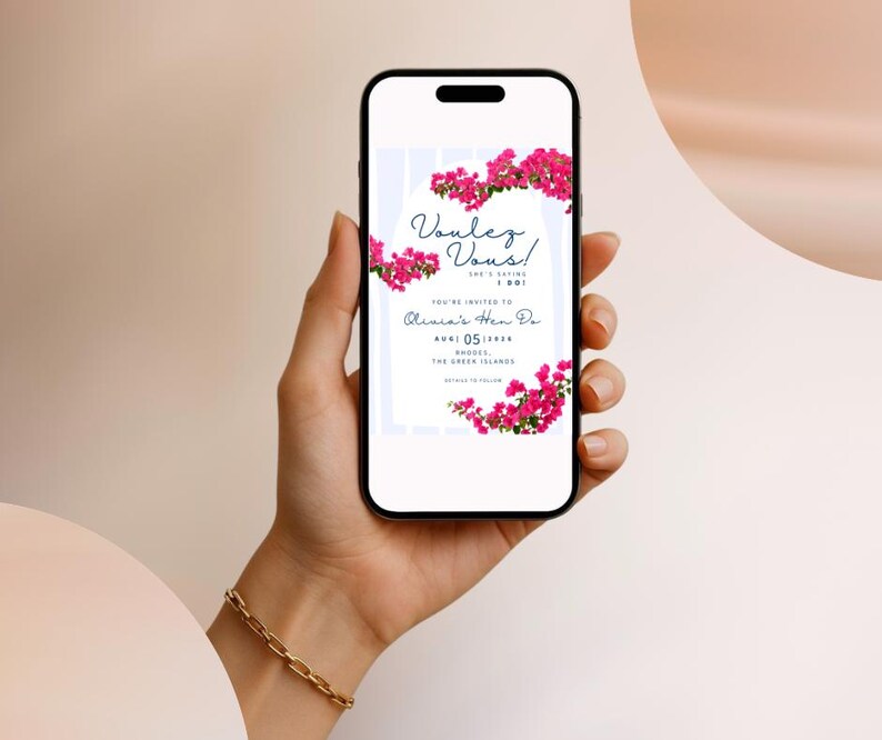 May include: A smartphone displays a digital invitation with the text "Voulez Vous!" and "Olivia's Hen Do". The invitation is decorated with pink flowers. The phone is held in a hand with a gold bracelet.