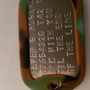 May include: A camouflage-colored dog tag with the text "STEVEN G. ROGERS  87654320  I'M WITH YOU  'TIL THE END  OF THE LINE" engraved on a silver metal plate.
