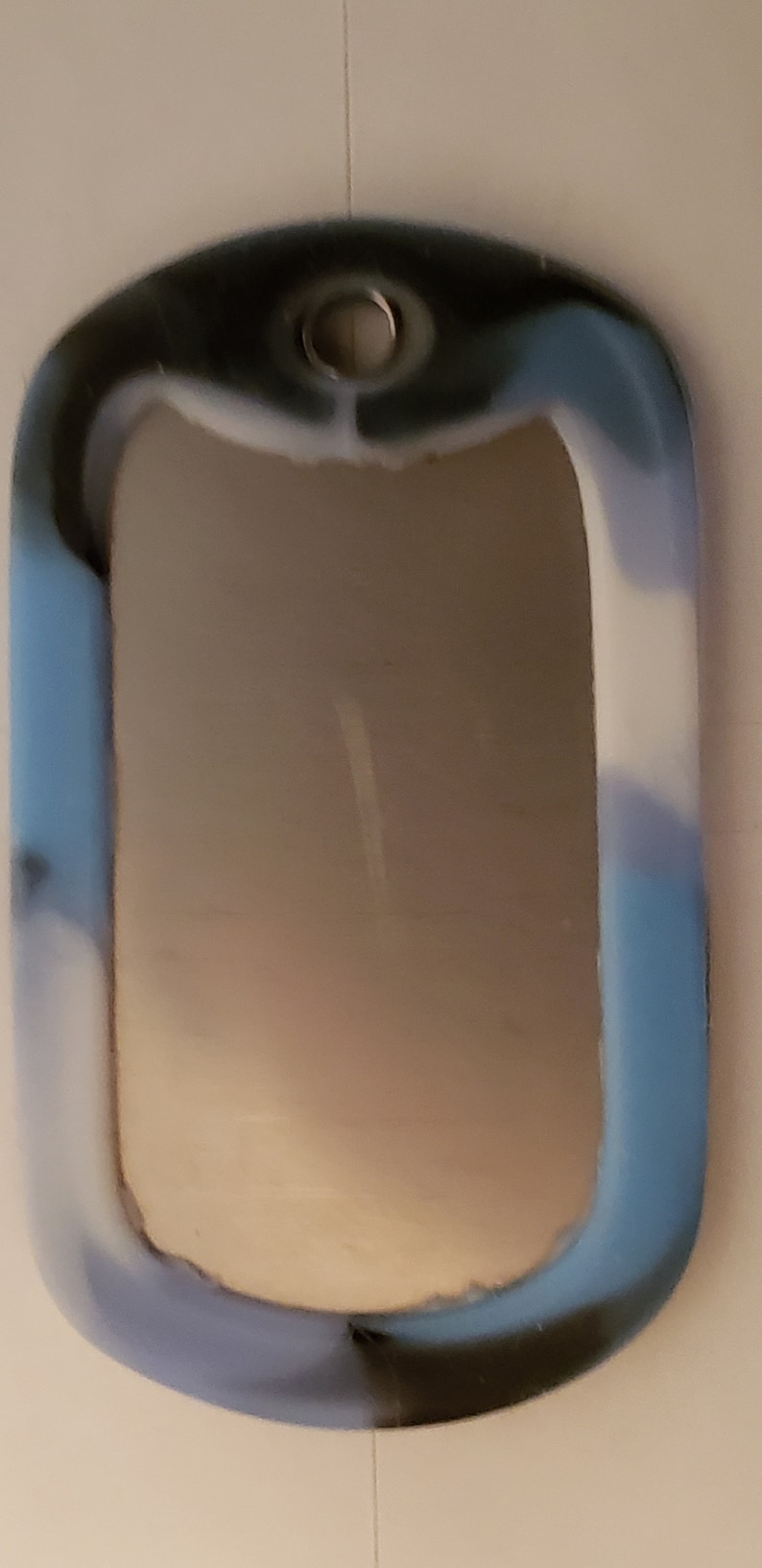 May include: A blue, black, and white camouflage dog tag with a silver ring.
