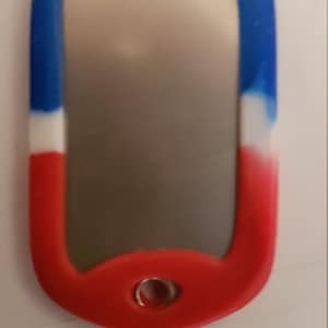 May include: A red, white, and blue silicone dog tag with a silver metal insert. The tag has a small hole at the top for attaching a chain or lanyard.