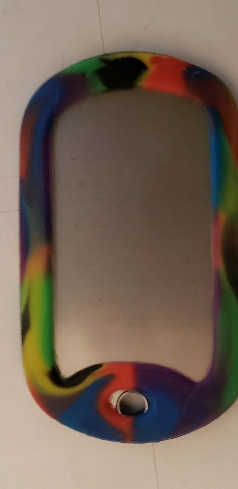 May include: A colorful, multi-colored, camouflage patterned dog tag with a silver metal insert and a round hole for a ring.