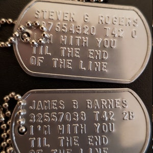 May include: Two silver dog tags on a silver chain. The top tag reads "STEVEN G ROGERS 87654320 T42 0 I'M WITH YOU TIL THE END OF THE LINE". The bottom tag reads "JAMES B BARNES 32557038 T42 2B I'M WITH YOU TIL THE END OF THE LINE".
