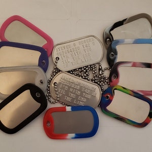 May include: A collection of silver dog tags with personalized engravings. The tags are attached to chains and some have colorful rubber covers. The engravings include names, numbers, and the phrase "I'm with you til the end of the line".