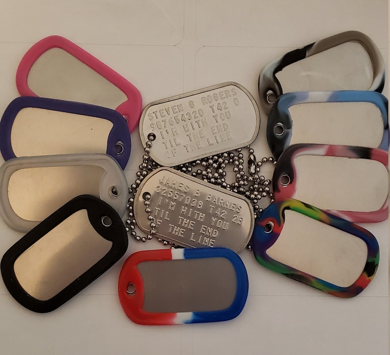 May include: A collection of silver dog tags with personalized engravings. The tags are attached to chains and some have colorful rubber covers. The engravings include names, numbers, and the phrase "I'm with you til the end of the line".