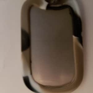 May include: A silver oval-shaped dog tag with a black, white, and brown camouflage pattern.