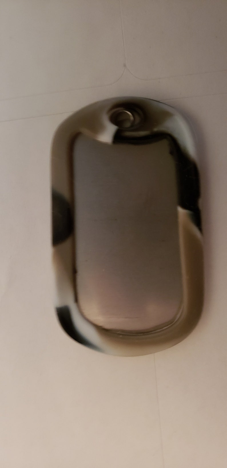 May include: A silver oval-shaped dog tag with a black, white, and brown camouflage pattern.