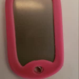 May include: A pink silicone dog tag with a silver metal insert. The tag has a hole at the top for attaching a chain or lanyard.