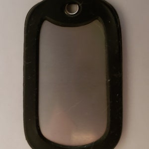May include: A black dog tag with a silver metal insert. The tag has a round hole at the top for attaching a chain.